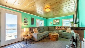 Un salon chaleureux avec un plafond en bois, un mur vert, une grande fenêtre, un canapé, une table basse et une cheminée.