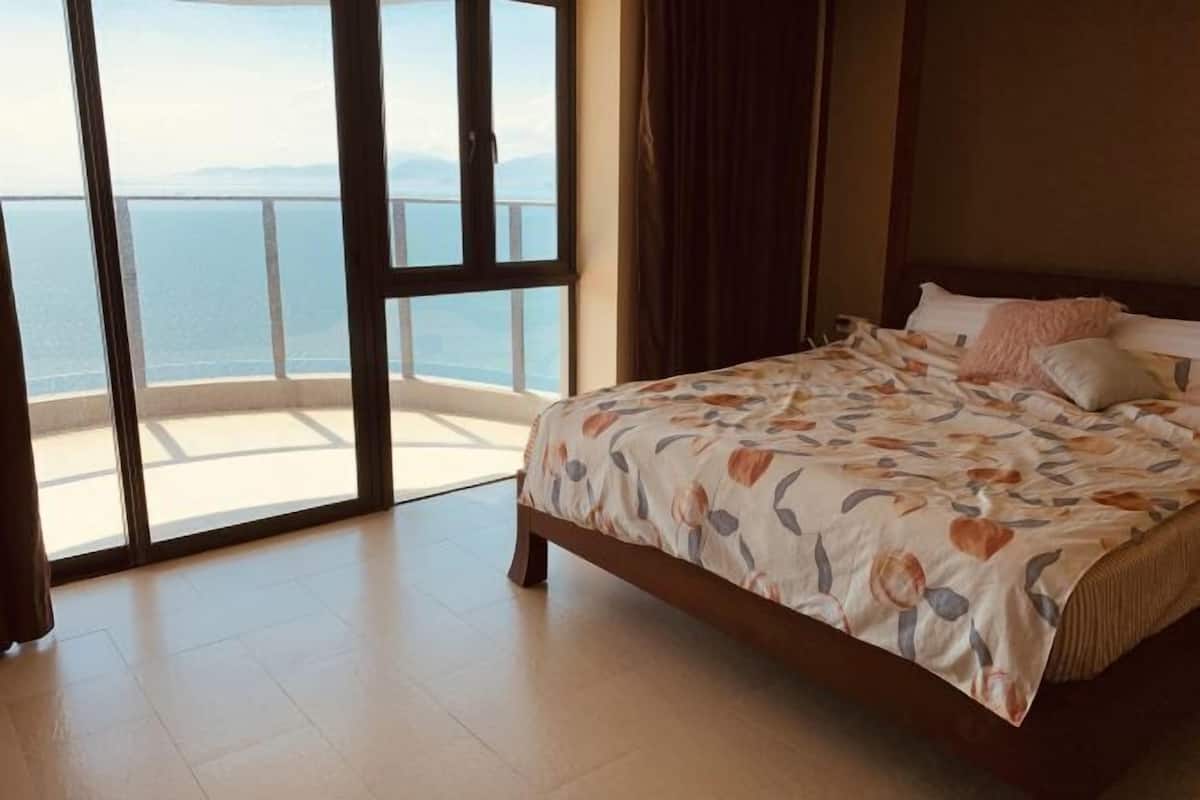 A bedroom with a large bed, a view of the sea, and a balcony.