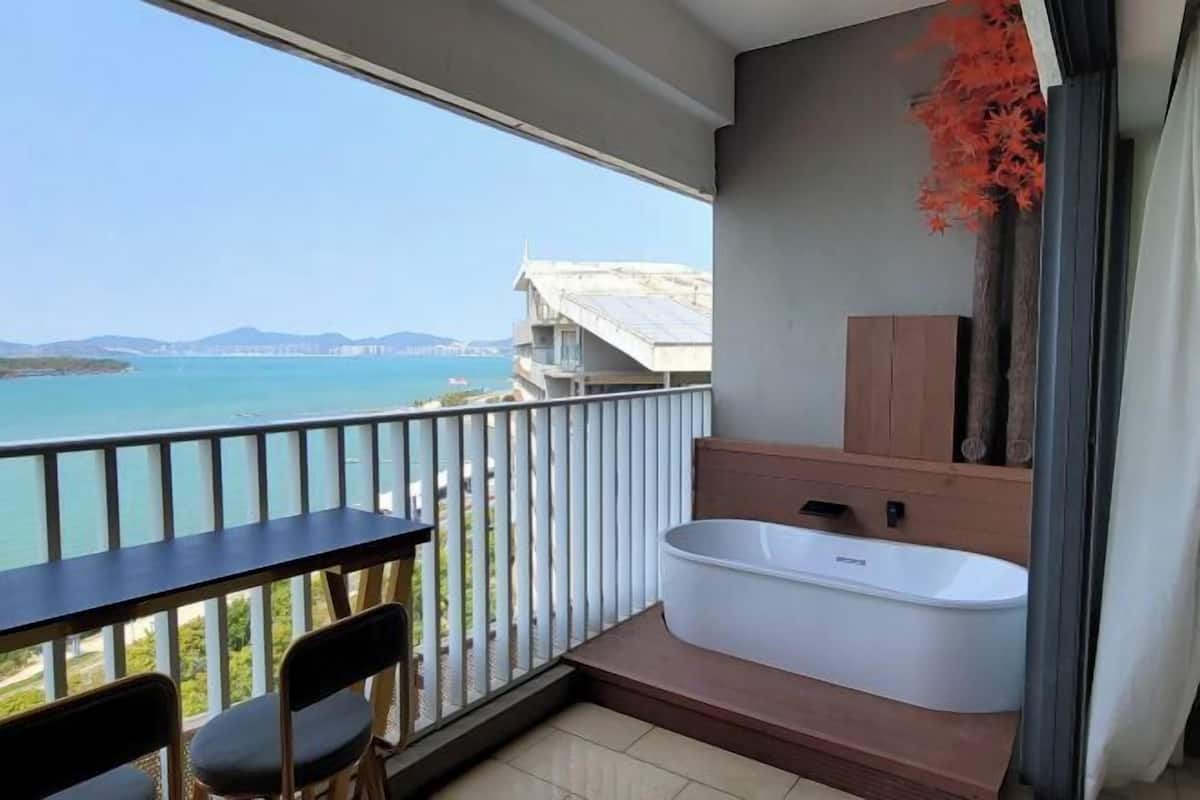 A balcony with a view of the sea, a bathtub, and a small table with chairs.