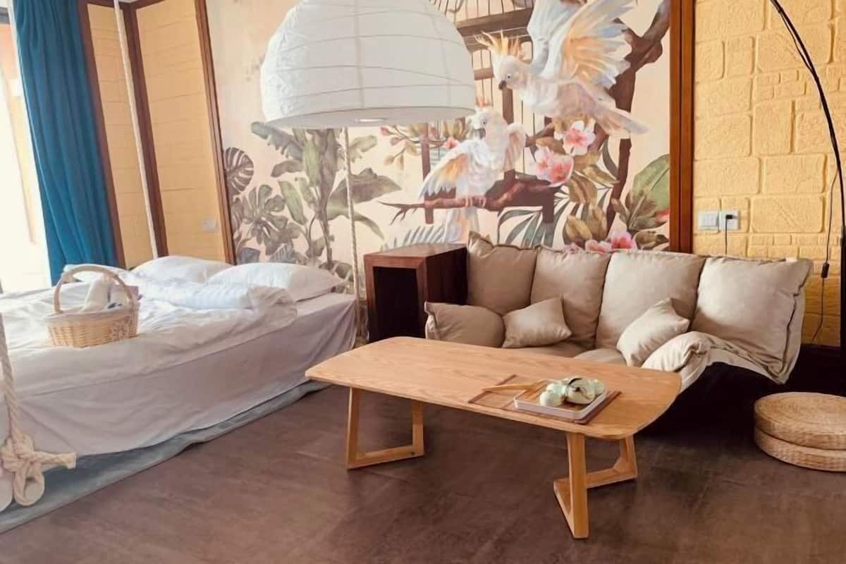 A room with a bed, a sofa, a wooden coffee table, and a wall mural.