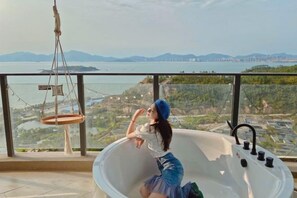 Une personne se détend dans une baignoire, avec vue sur une étendue d’eau et sur une terre lointaine.