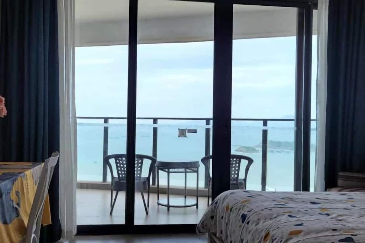 A hotel room with a bed, a table, and a balcony with a view of the sea.
