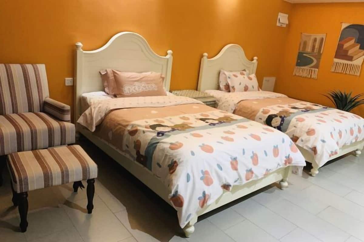A bedroom with two beds, a striped chair, and a bench.