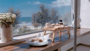 A wooden table with a vase of flowers, a plate with cookies, and a tray with cups and a teapot by a window overlooking the sea. - Huidong Sumao Homestay (Xunliao Bay) (Huidong)