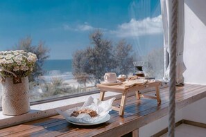 A wooden table with a vase of flowers, a plate with cookies, and a tray with cups and a teapot by a window overlooking the sea. - Huidong Sumao Homestay (Xunliao Bay) (Huidong)
