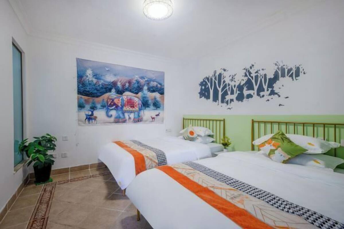 A hotel room with two beds, a painting on the wall, and a decorative tree decal.