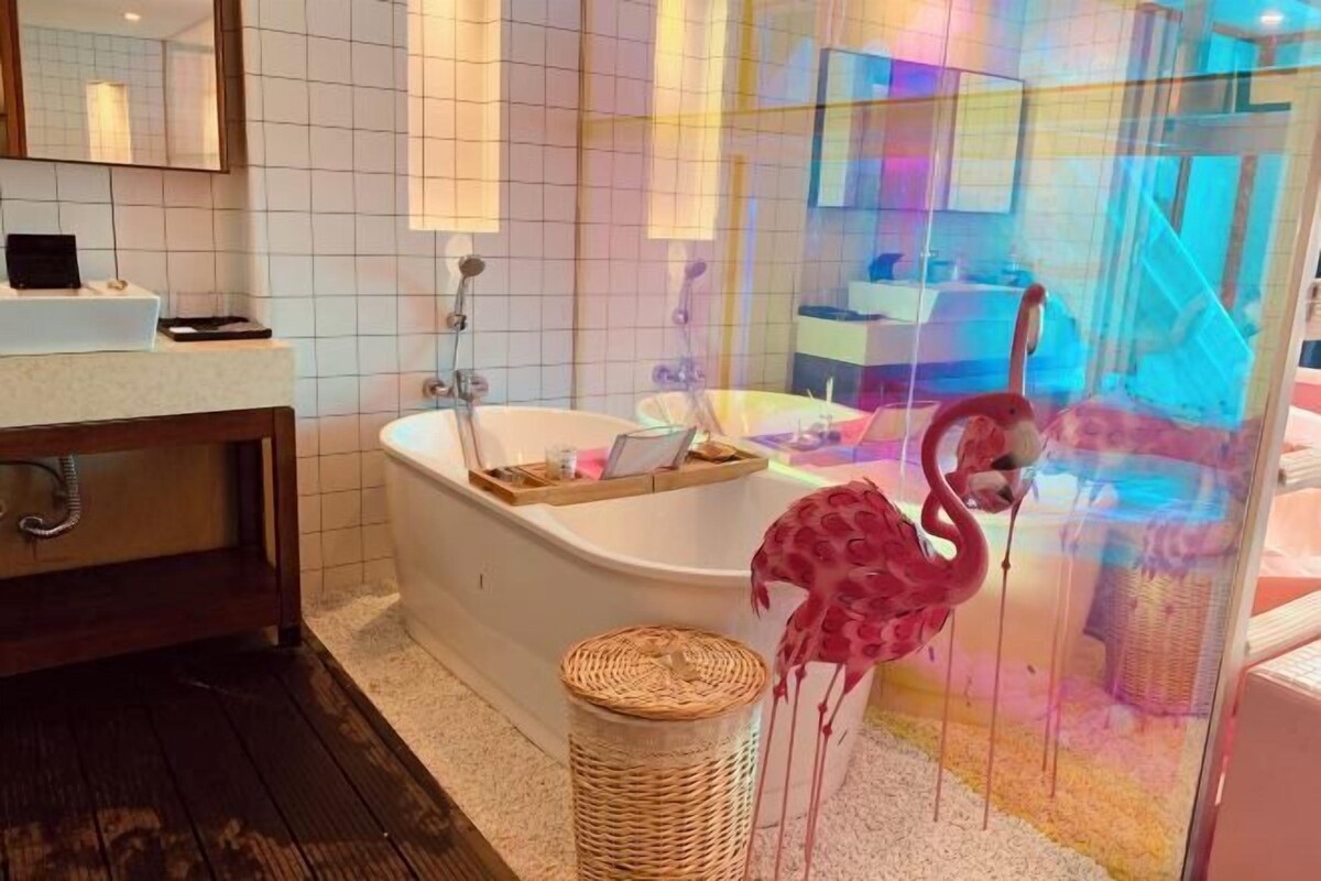 A bathroom with a bathtub, a wooden vanity, a wicker basket, and a glass enclosure with a flamingo decoration.