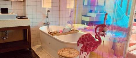 A bathroom with a bathtub, a wooden vanity, a wicker basket, and a glass enclosure with a flamingo decoration.