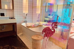 A bathroom with a bathtub, a wooden vanity, a wicker basket, and a glass enclosure with a flamingo decoration. - Huidong Sumao Homestay (Xunliao Bay) (Huidong)
