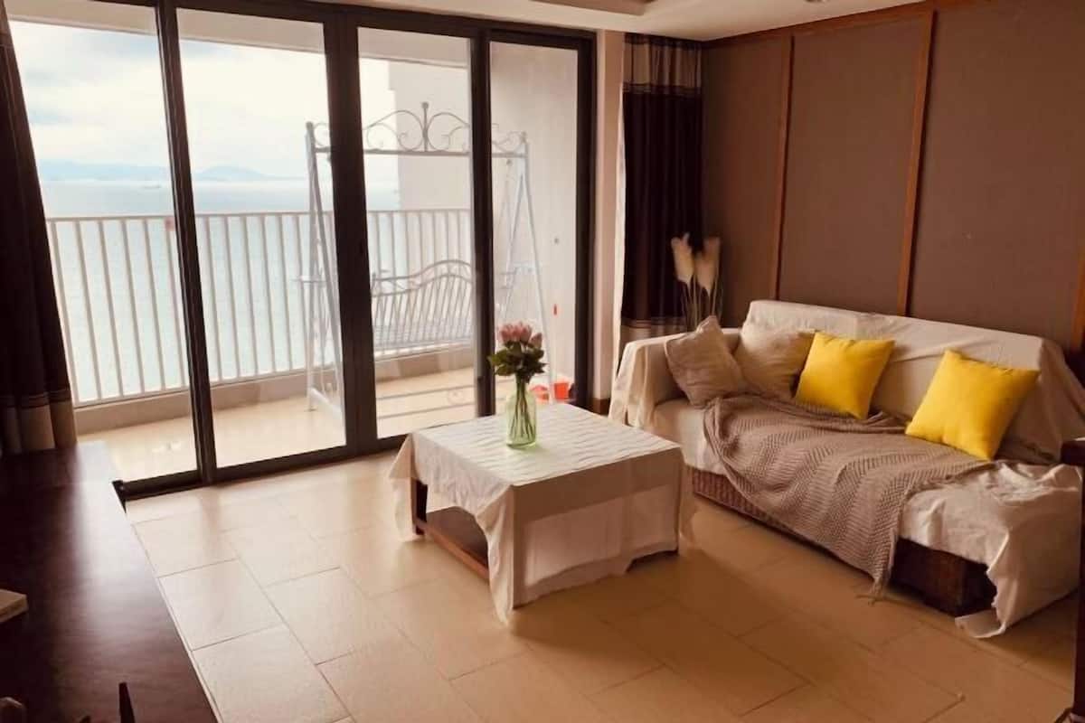 A room with a sofa, a table, and a view of the balcony.