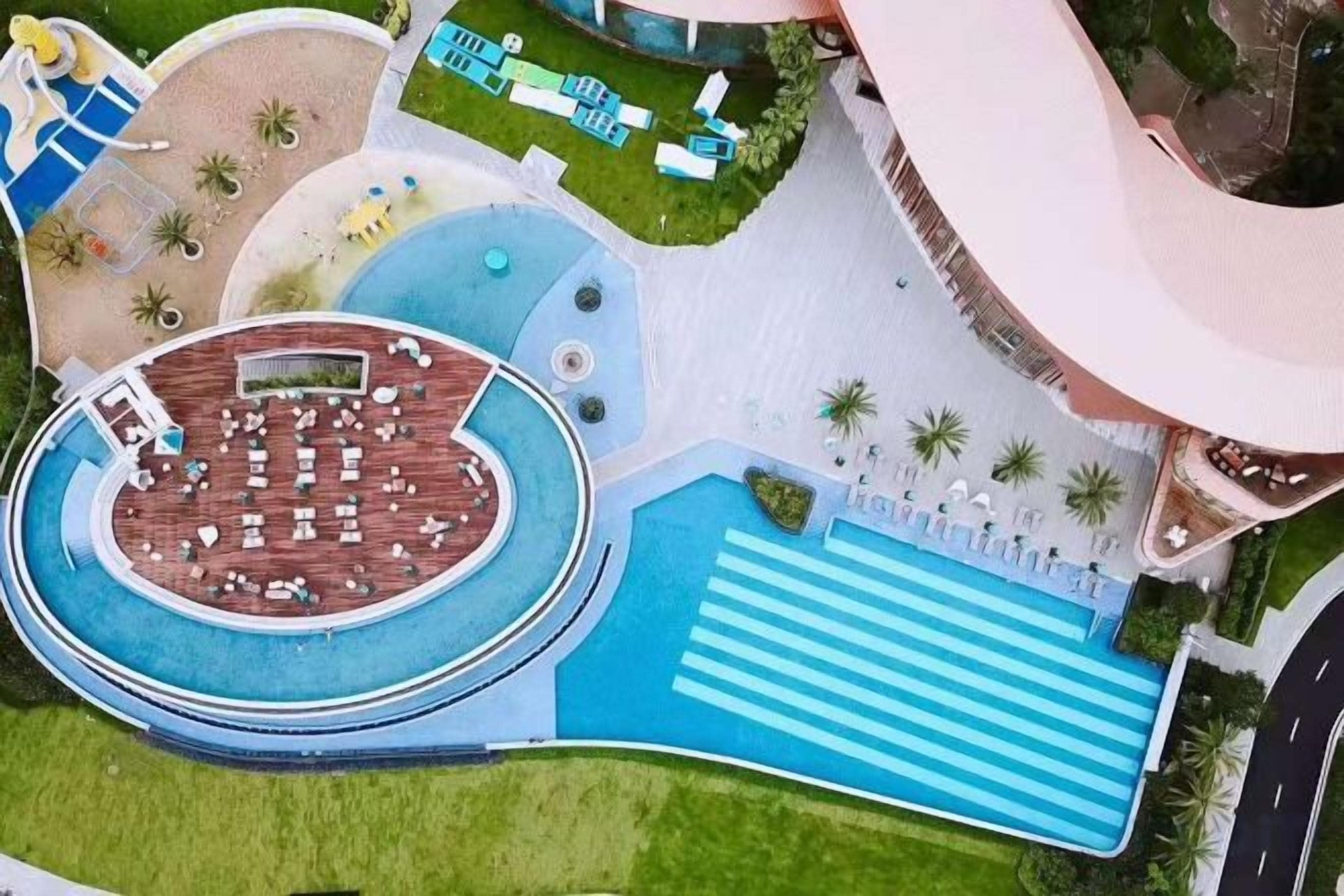 Vista aerea di un resort con una grande piscina, uno scivolo acquatico e un’area solarium circolare.