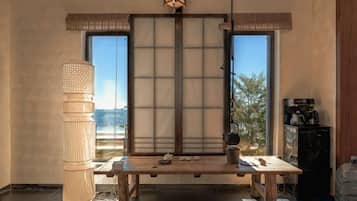 A traditional Japanese room with tatami flooring, a low table, a shoji screen, and a large window with a view.