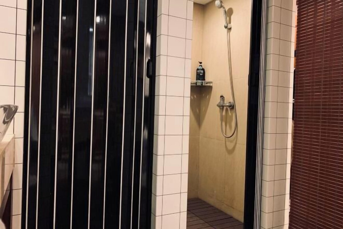 A bathroom with a shower, tiled walls, and a black door.