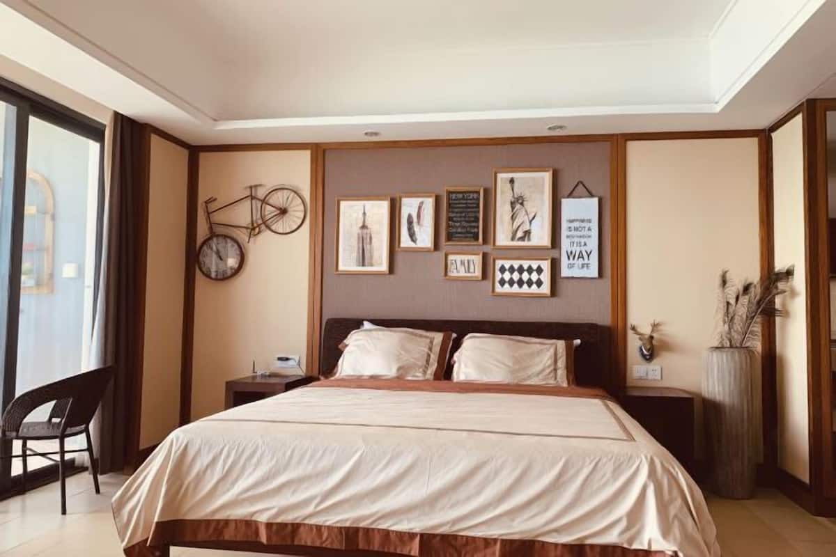 A hotel room with a large bed, a nightstand, a chair, and wall art including a bicycle, cityscape, and a quote.