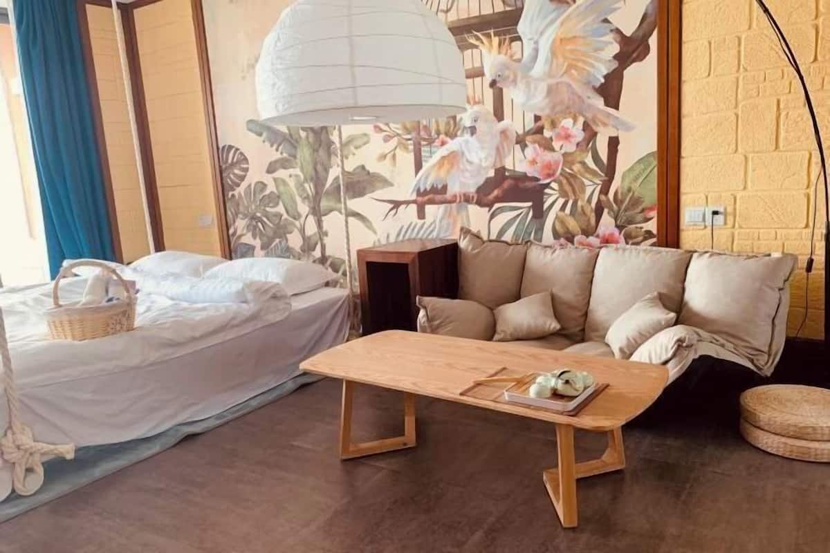 A room with a bed, a sofa, a wooden table, and a wall mural.
