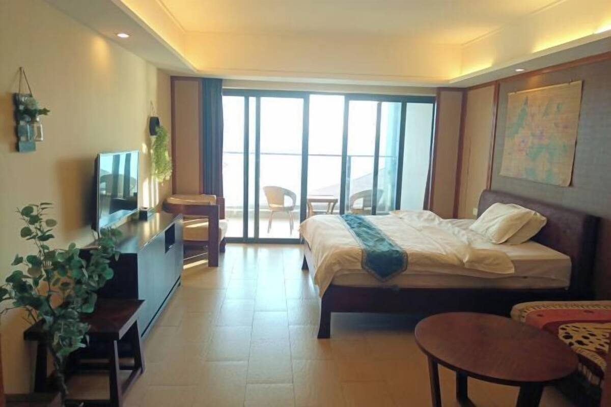 A hotel room with a bed, a desk, a chair, a small table, and a balcony with a view.