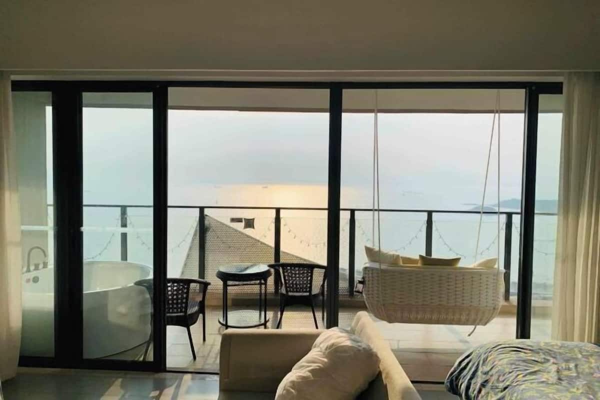 A modern hotel room with a balcony, a bathtub, and a hanging chair.