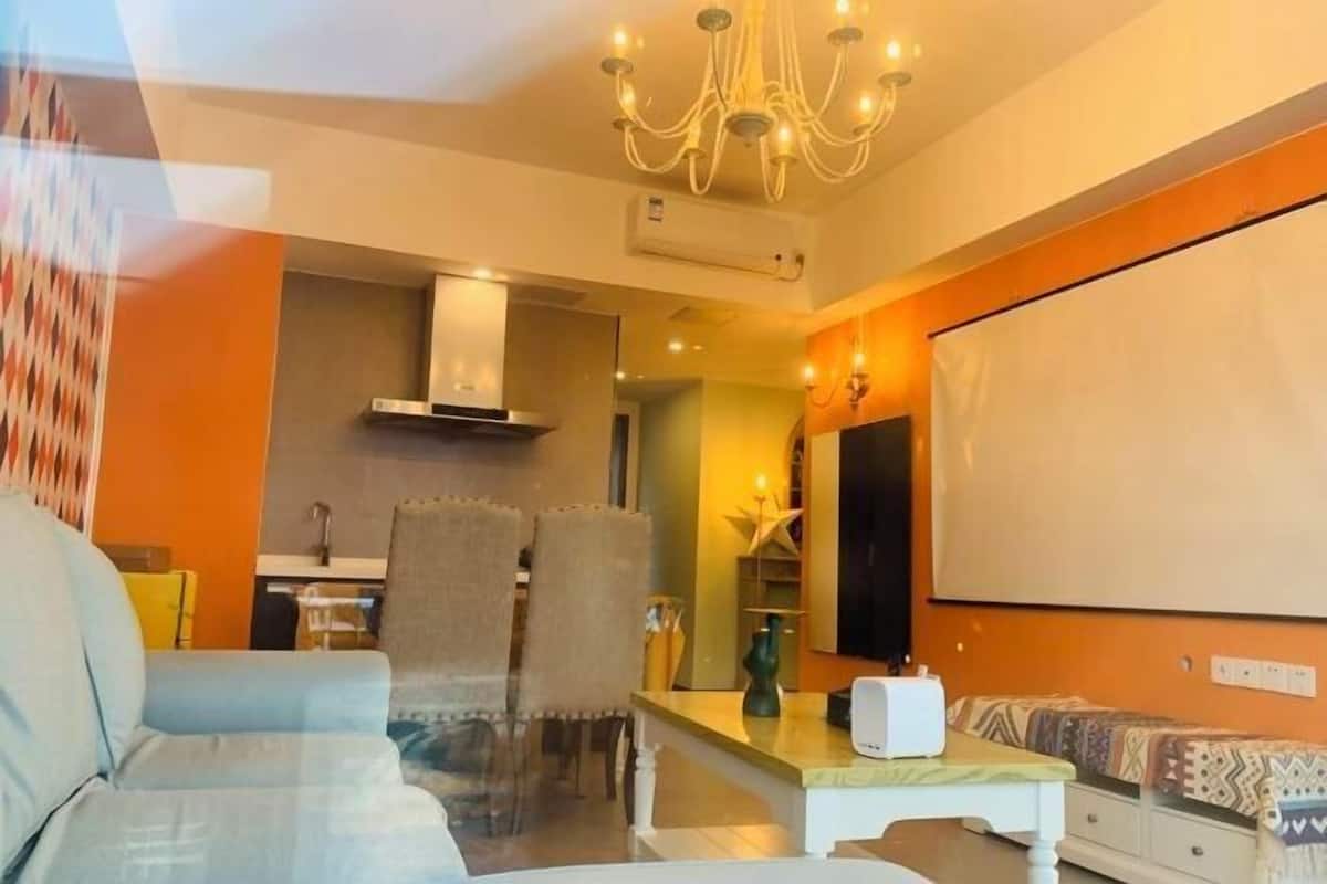 A living room with a sofa, a coffee table, a TV, and a kitchen area in the background.