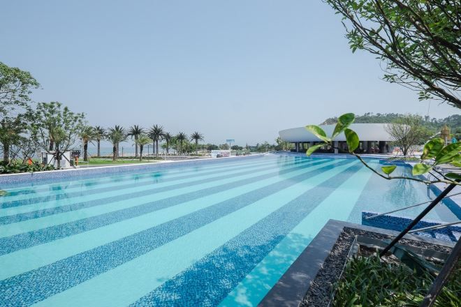 A swimming pool with a clear blue water feature, surrounded by greenery and a building in the background.