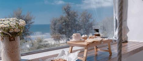 A wooden table with a vase of flowers, a plate with cookies, and a cup on a balcony overlooking the sea.