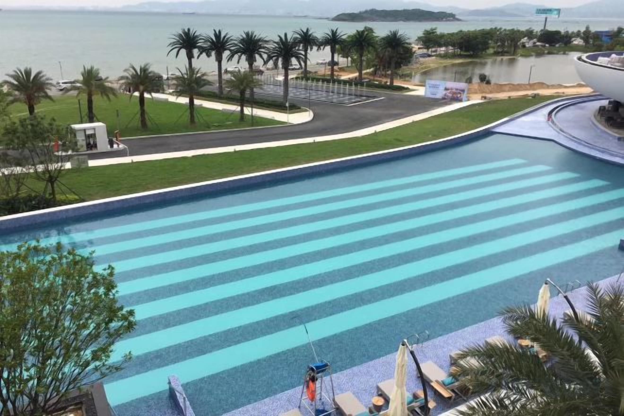 A large swimming pool with a view of the sea and palm trees.