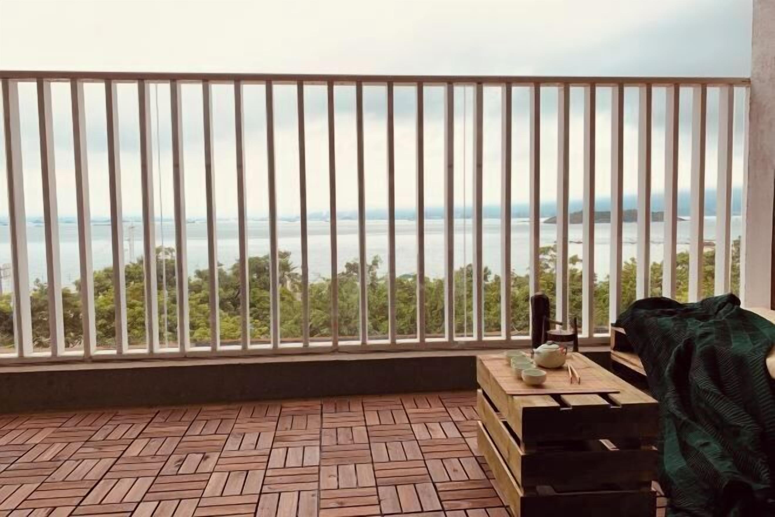 Varanda com vista para o mar, piso de madeira, mesa com cadeira e um cobertor.