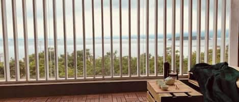 Un balcon avec vue sur la mer, un plancher en bois, une table avec une chaise et une couverture.