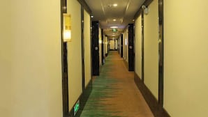 A hotel hallway with carpeted floors, doors on both sides, and a light fixture on the left wall.