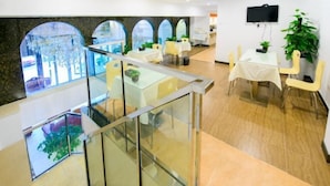 A hotel lobby with a glass railing, tables, chairs, and a TV on the wall.