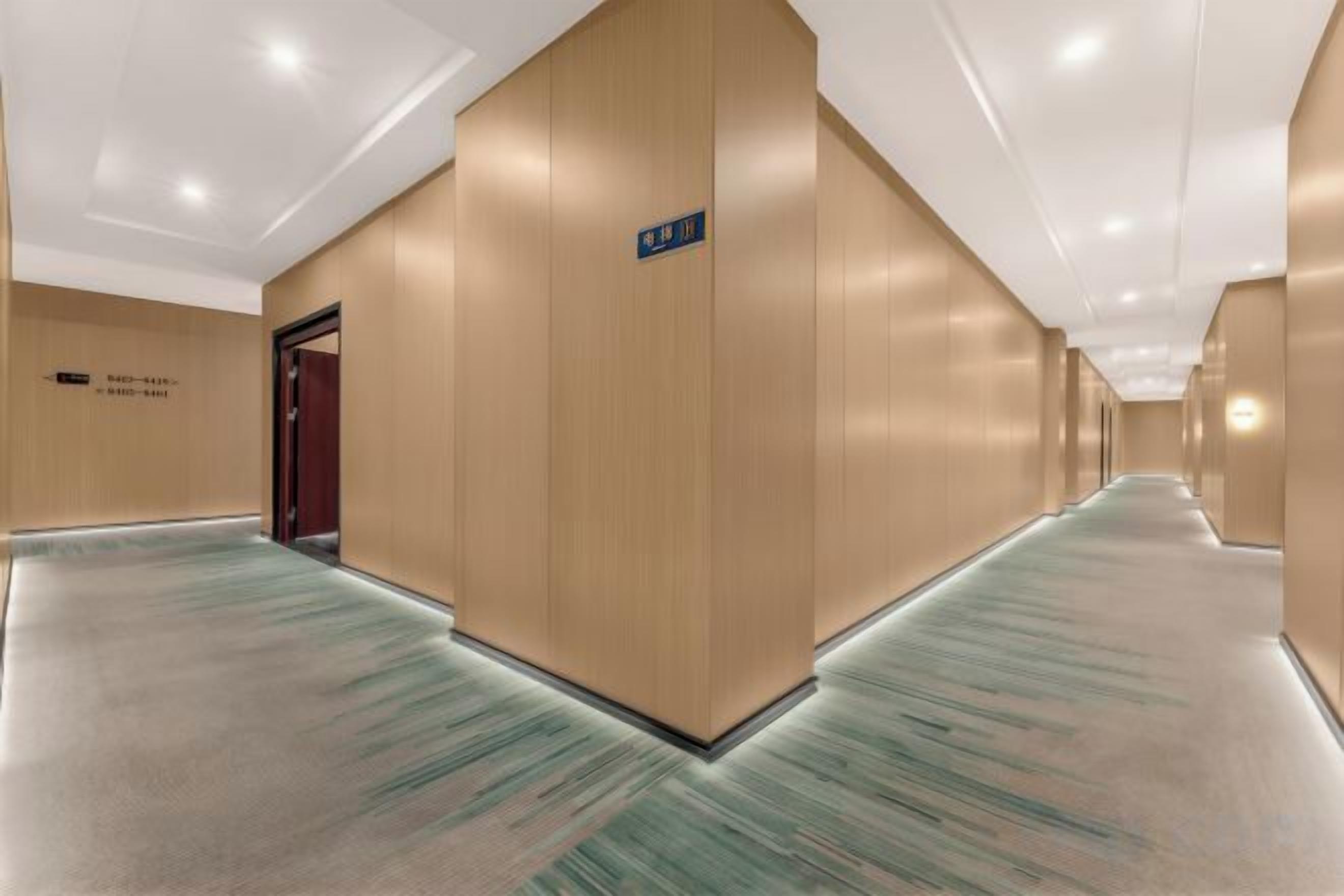 A hotel corridor with a carpeted floor, wooden walls, and a door on the left.