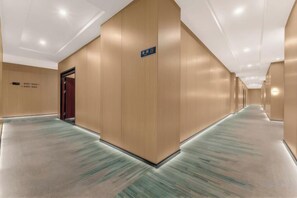 Un pasillo de hotel con suelo alfombrado, paredes de madera y una puerta a la izquierda.