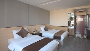 A hotel room with two beds, a small desk, a mirror, and a bathroom door.