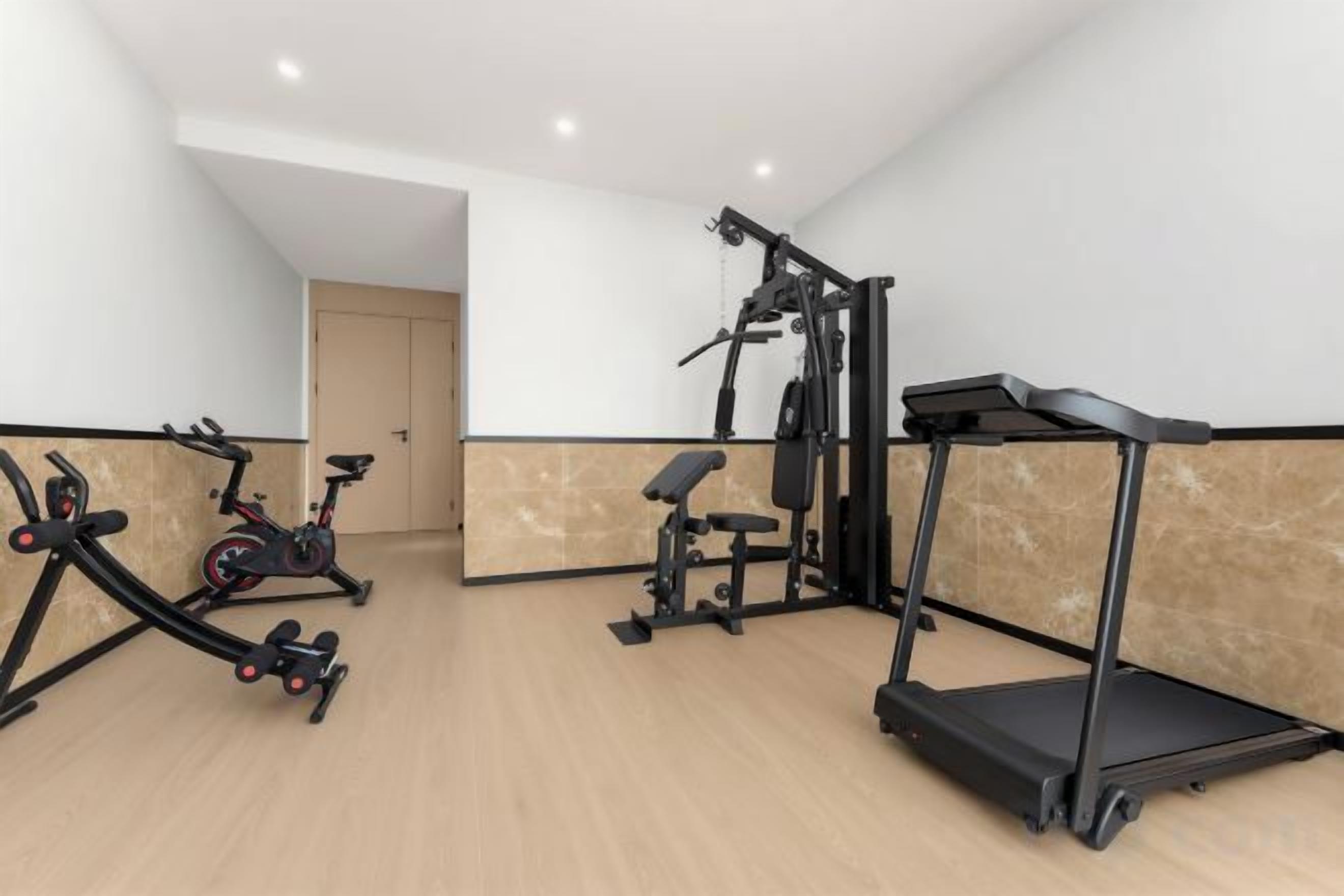 A gym with exercise equipment including a treadmill, elliptical, and weight machines.