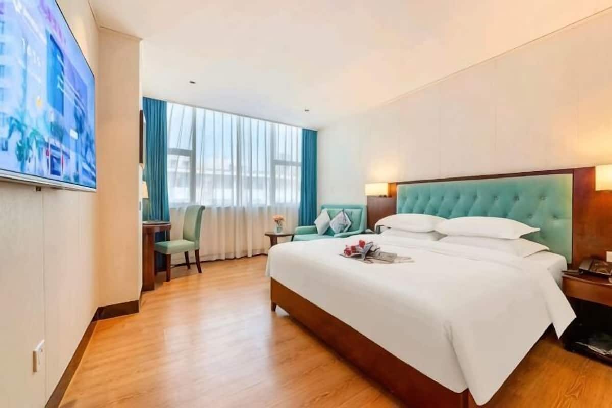 A hotel room with a large bed, a desk, a chair, a TV, and a window with curtains.