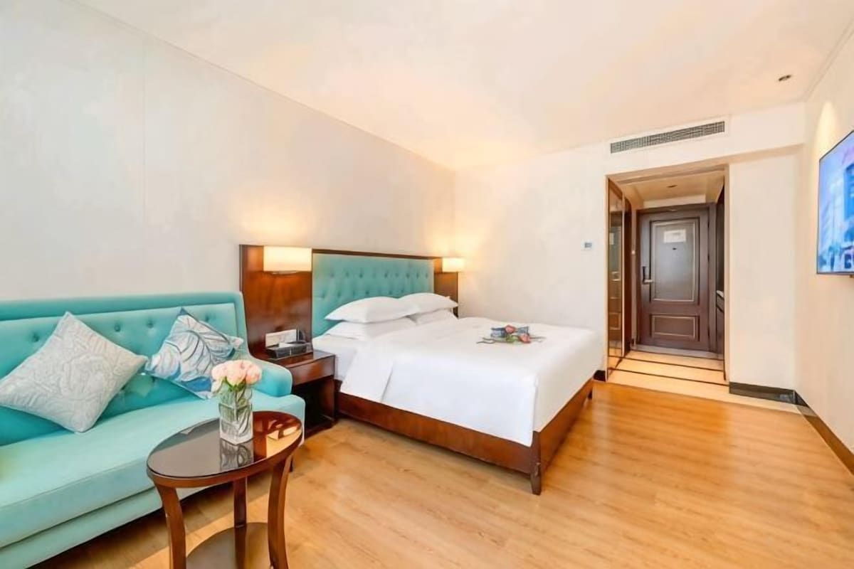 A hotel room with a bed, a sofa, a small table, and a door leading to another room.