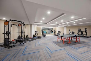 A gym with exercise equipment, a ping pong table, and a view of the lobby.