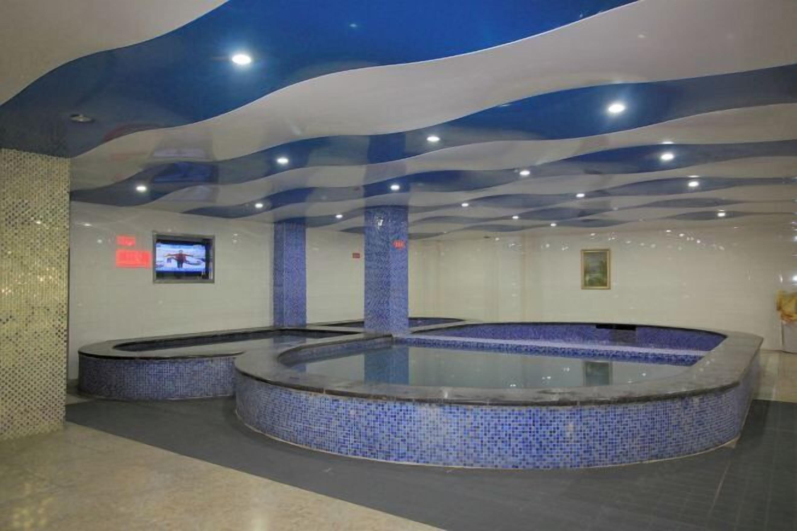 A modern indoor swimming pool with blue mosaic tiles and a wavy ceiling design.