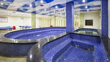 Een groot binnenzwembad met een golvend ontwerp, omgeven door blauwe betegelde muren en een plafond met een golfpatroon.