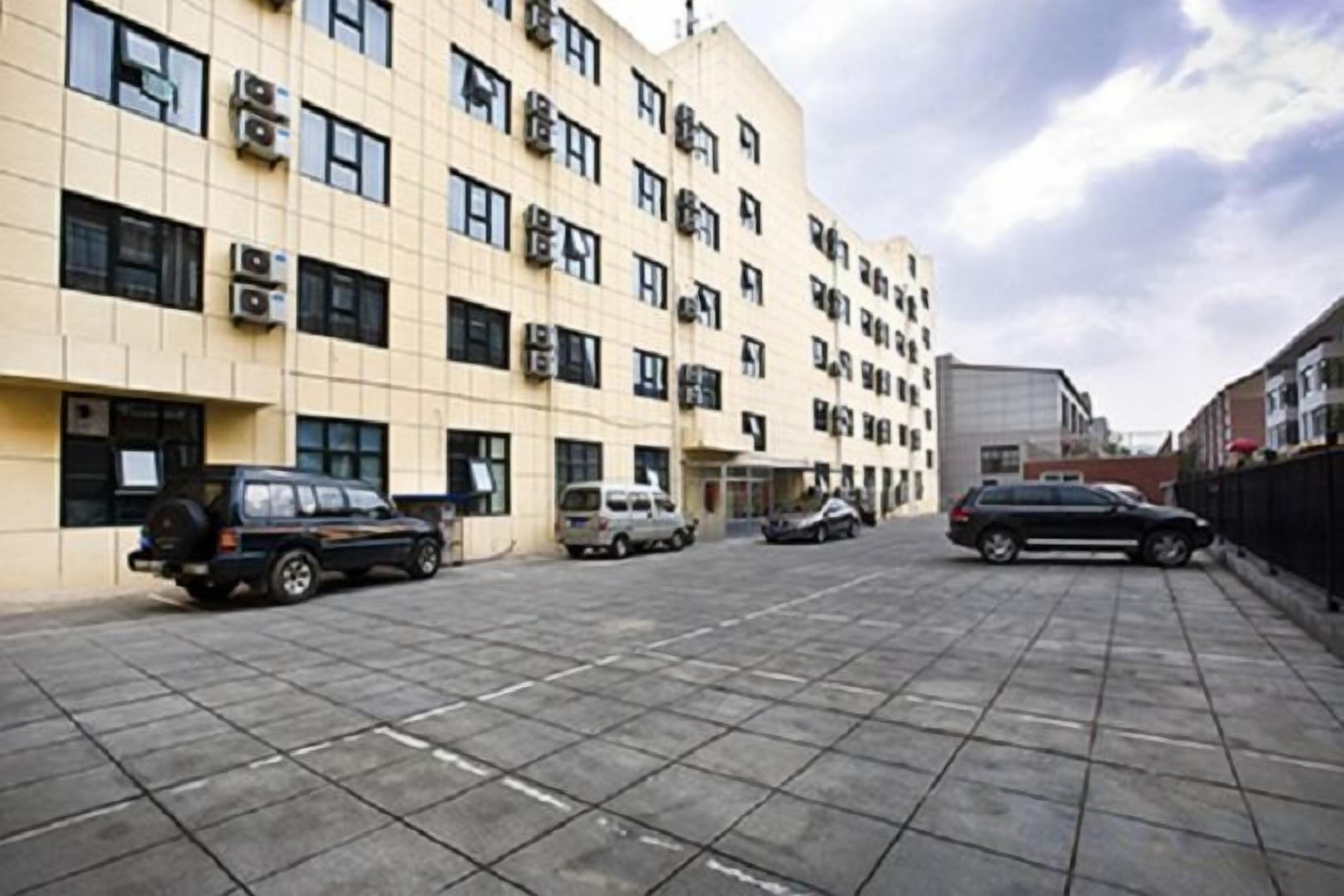 A parking lot with multiple cars parked in front of a building with multiple windows and air conditioning units.