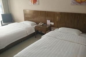 A hotel room with two beds, a wooden headboard, a bedside table with a phone, and a chair. - Longdu Business Hotel (Zhaoyuan)