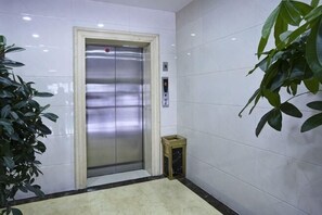 An elevator in a hallway with white walls and a potted plant. - Longdu Business Hotel (Zhaoyuan)