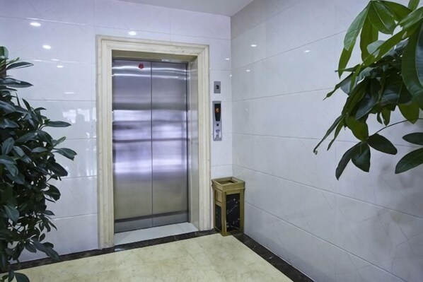 An elevator in a hallway with white walls and a potted plant. - Longdu Business Hotel (Zhaoyuan)