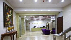 A reception area with a reception desk, purple seating, and a painting on the wall. - Longdu Business Hotel (Zhaoyuan)