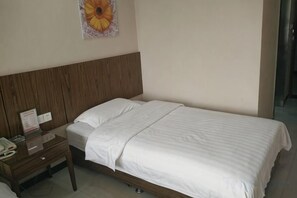 Un lit simple avec une tête de lit en bois, une table de chevet avec une lampe et une décoration florale fixée au mur.