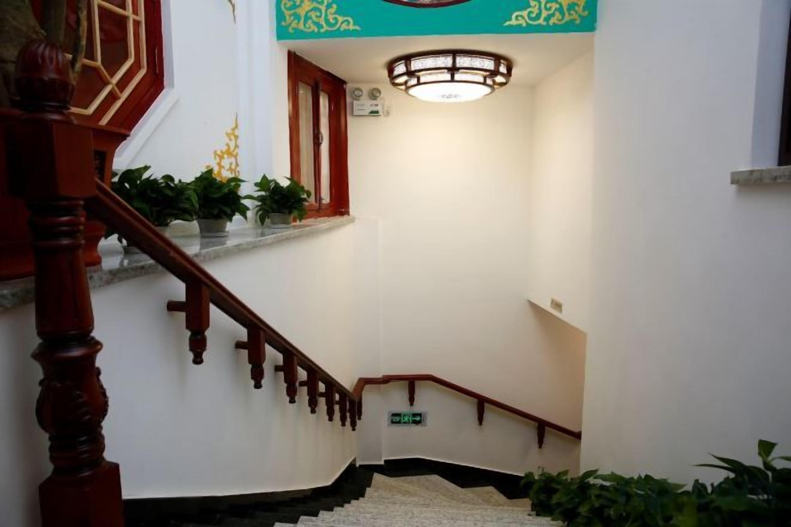 A staircase with a wooden handrail, a light fixture above, and potted plants on the landing.