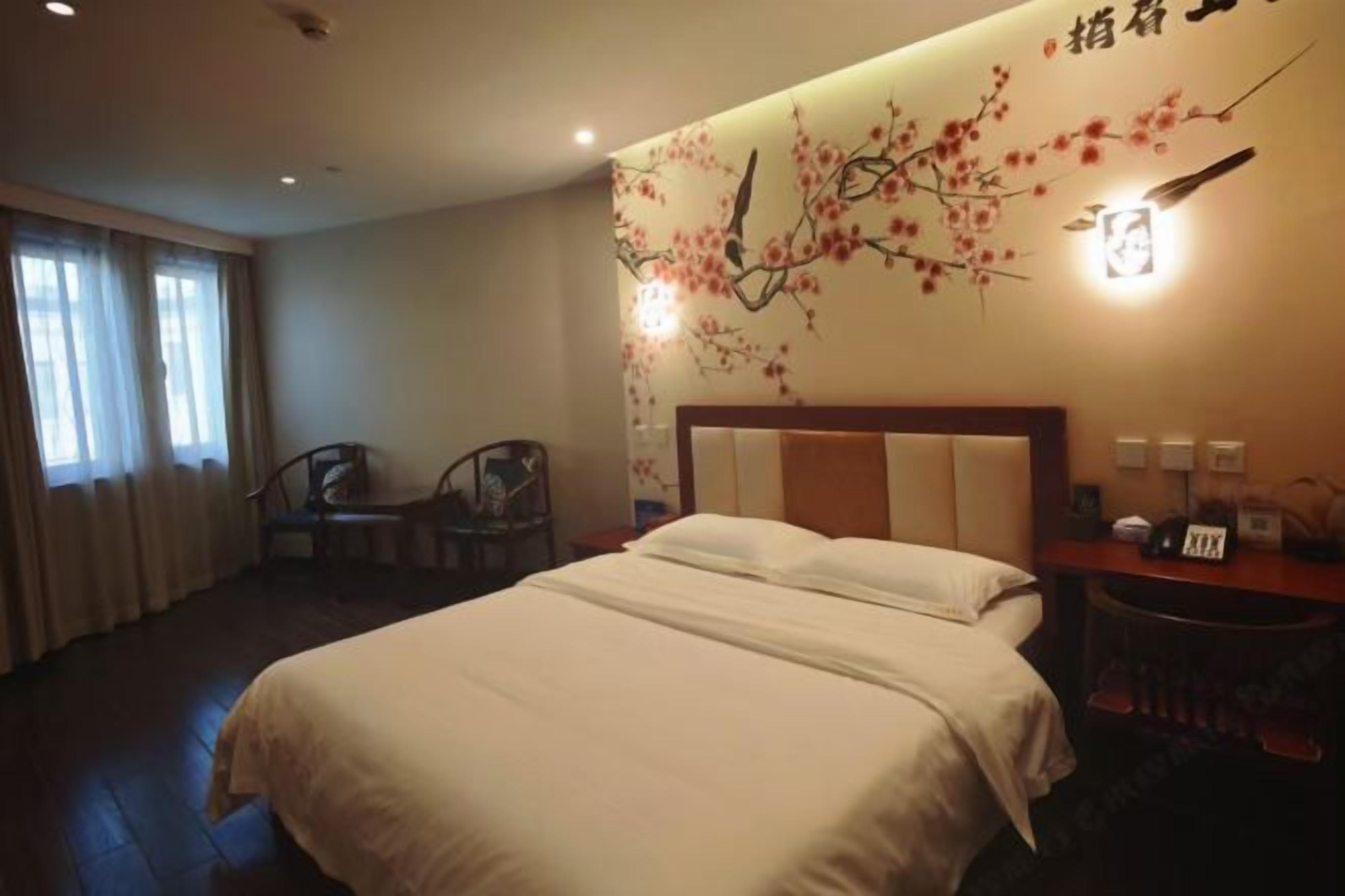 A hotel room with a bed, a desk, a chair, and a wall with a decorative branch design.