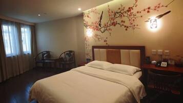 A hotel room with a bed, a desk, a chair, and a wall with a decorative branch design.
