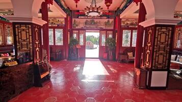 Interior de arquitectura tradicional china con un espacio central abierto, suelo de tejas rojas y paneles de madera decorativos.