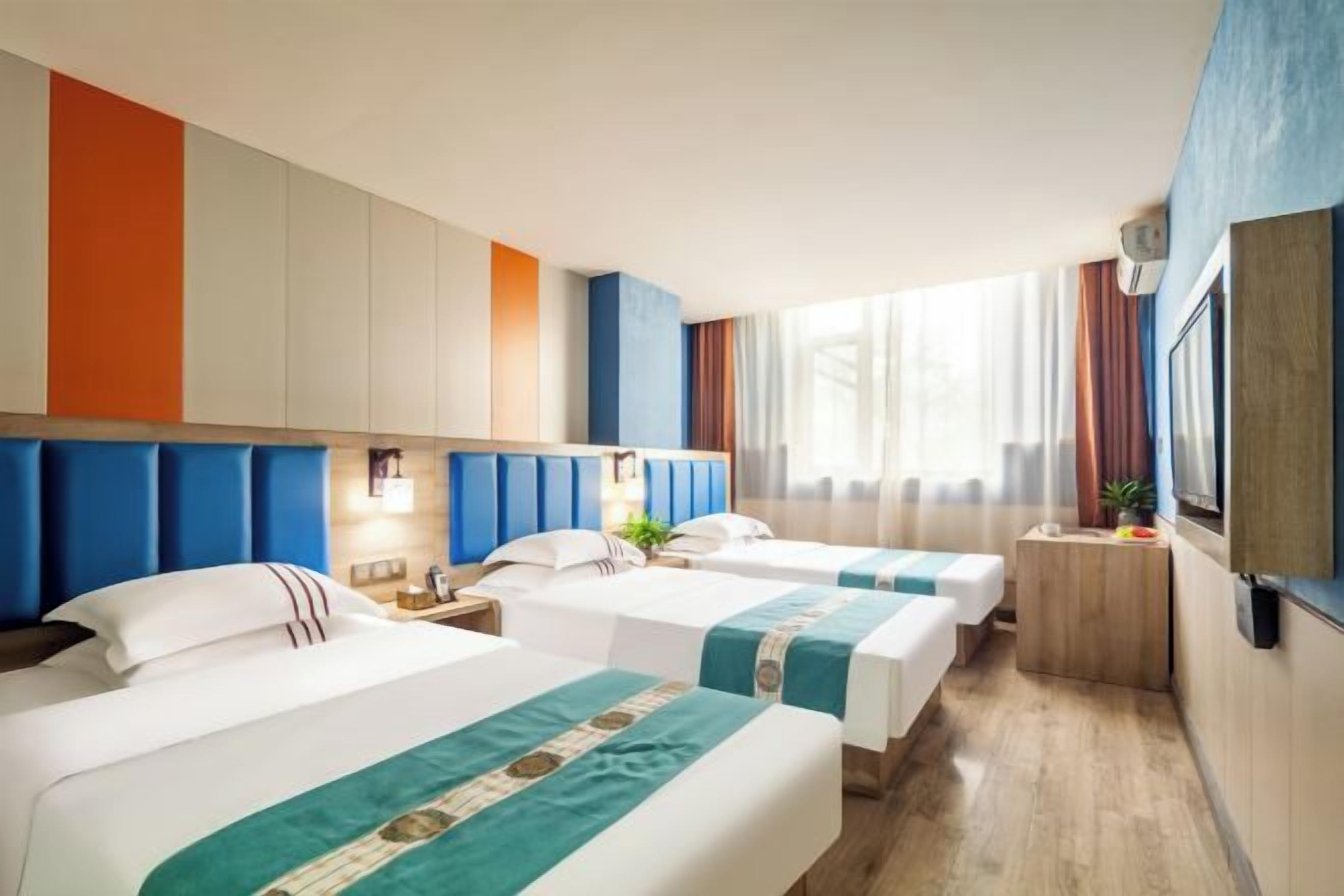 A hotel room with three beds, a small desk, a TV, and a window with curtains.