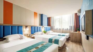 A hotel room with three beds, a small desk, a TV, and a window with curtains.